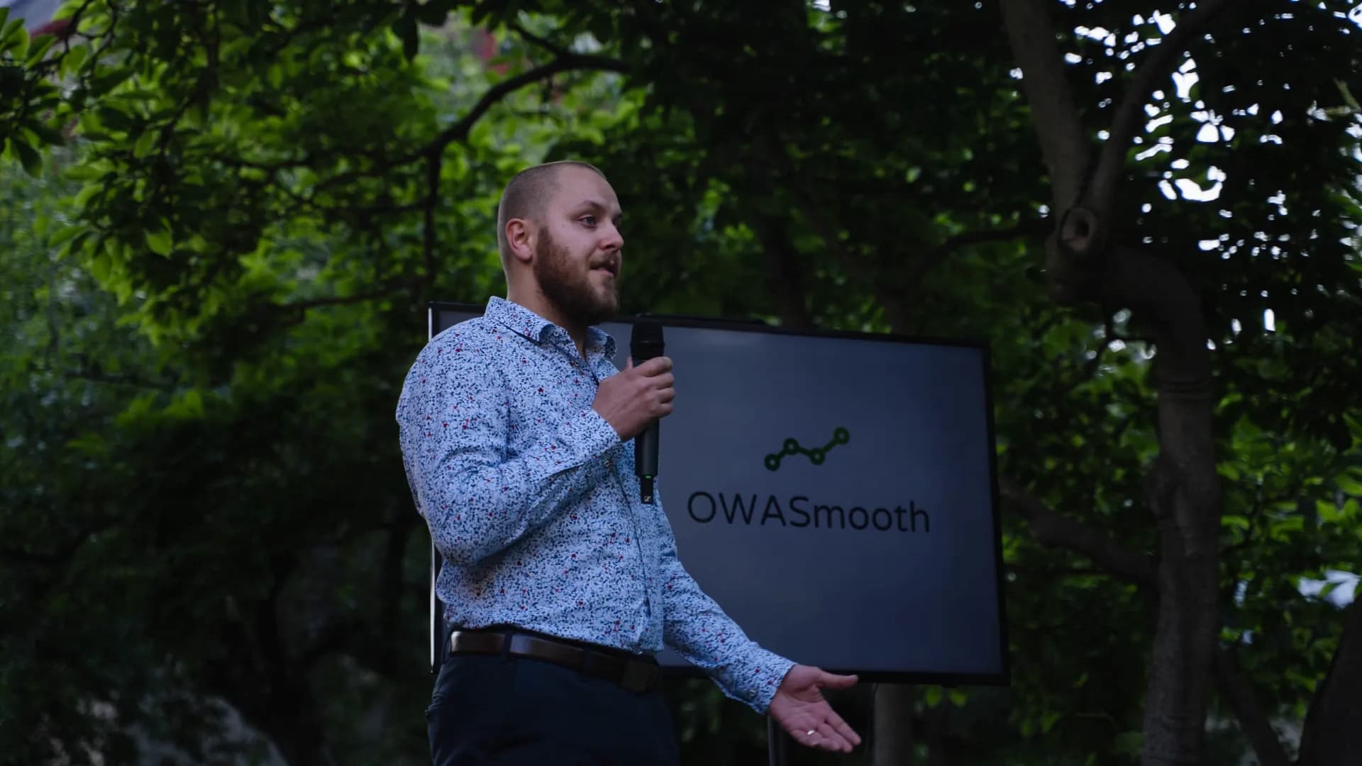 Founder Miro having a speech before the Czech Founder with a lush green background and the OWASmooth logo